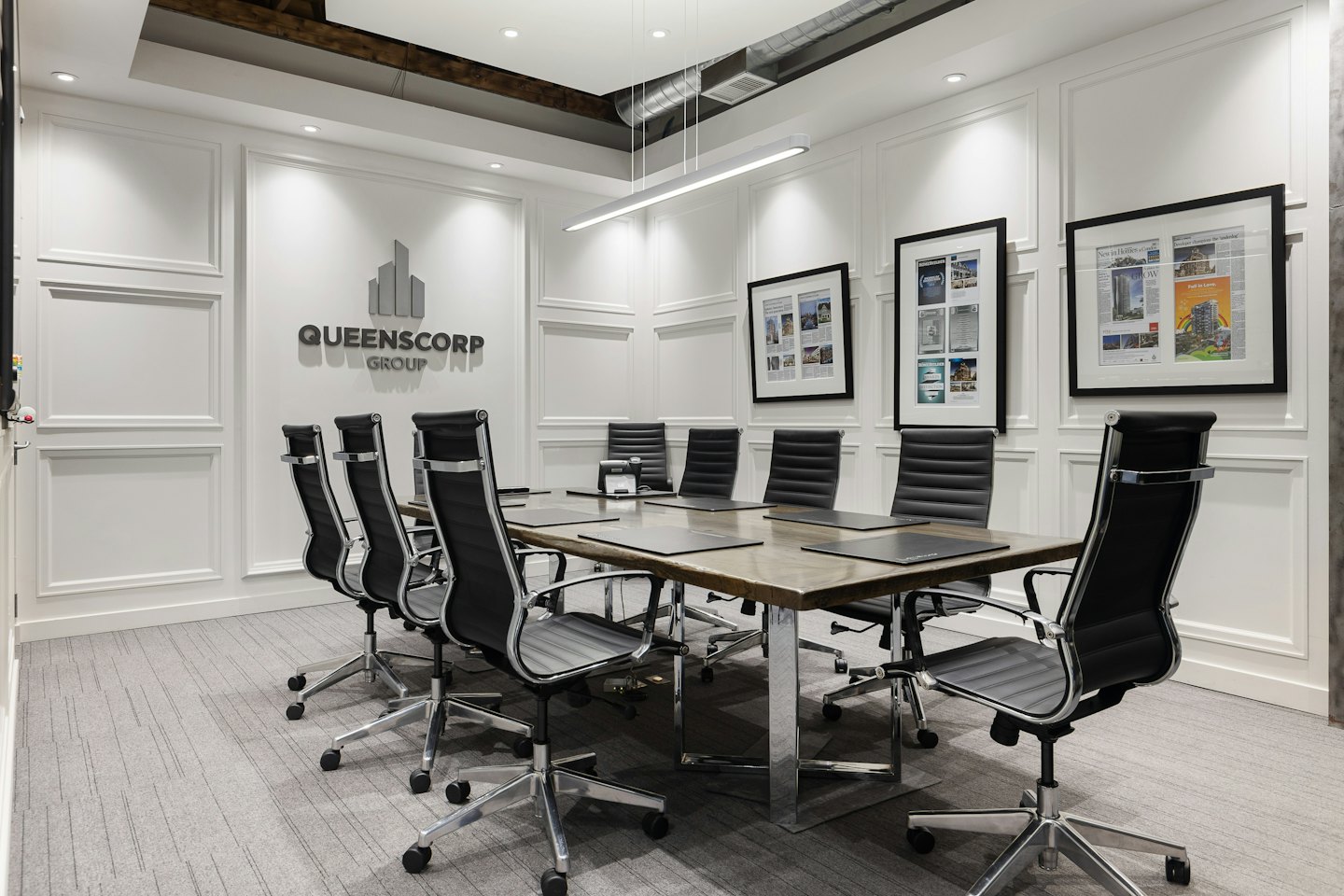 Sala de conferencias con mesa larga y el logo de Queenscorp Group.